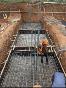 Slide 1 — Construction site showing workers setting up steel reinforcement bars in a foundation pit, surrounded by earth and wooden supports.