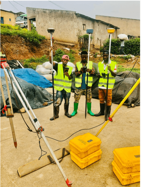 Slide 4 — Three workers in reflective vests and boots stand on a construction site, holding surveying equipment amidst a backdrop of equipment and greenery.